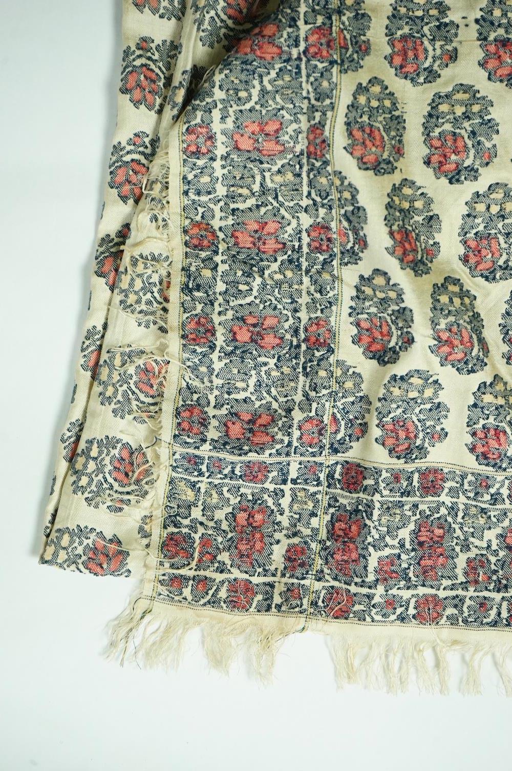 A 19th century silk woven shawl. Woven with a cream silk ground, with indigo, red and yellow, floral stylistic Buta motifs and bordered with three rows of a similar floral vining pattern. The edges fringed. 148cm x 152cm